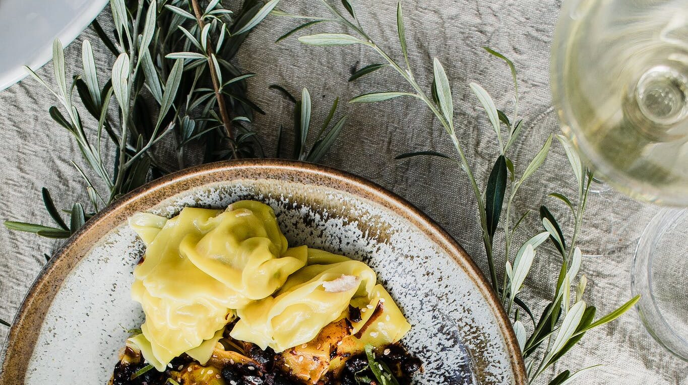 Top view of bowl with tasty homemade pasta served on table near glass and plates and decorated with green herbs