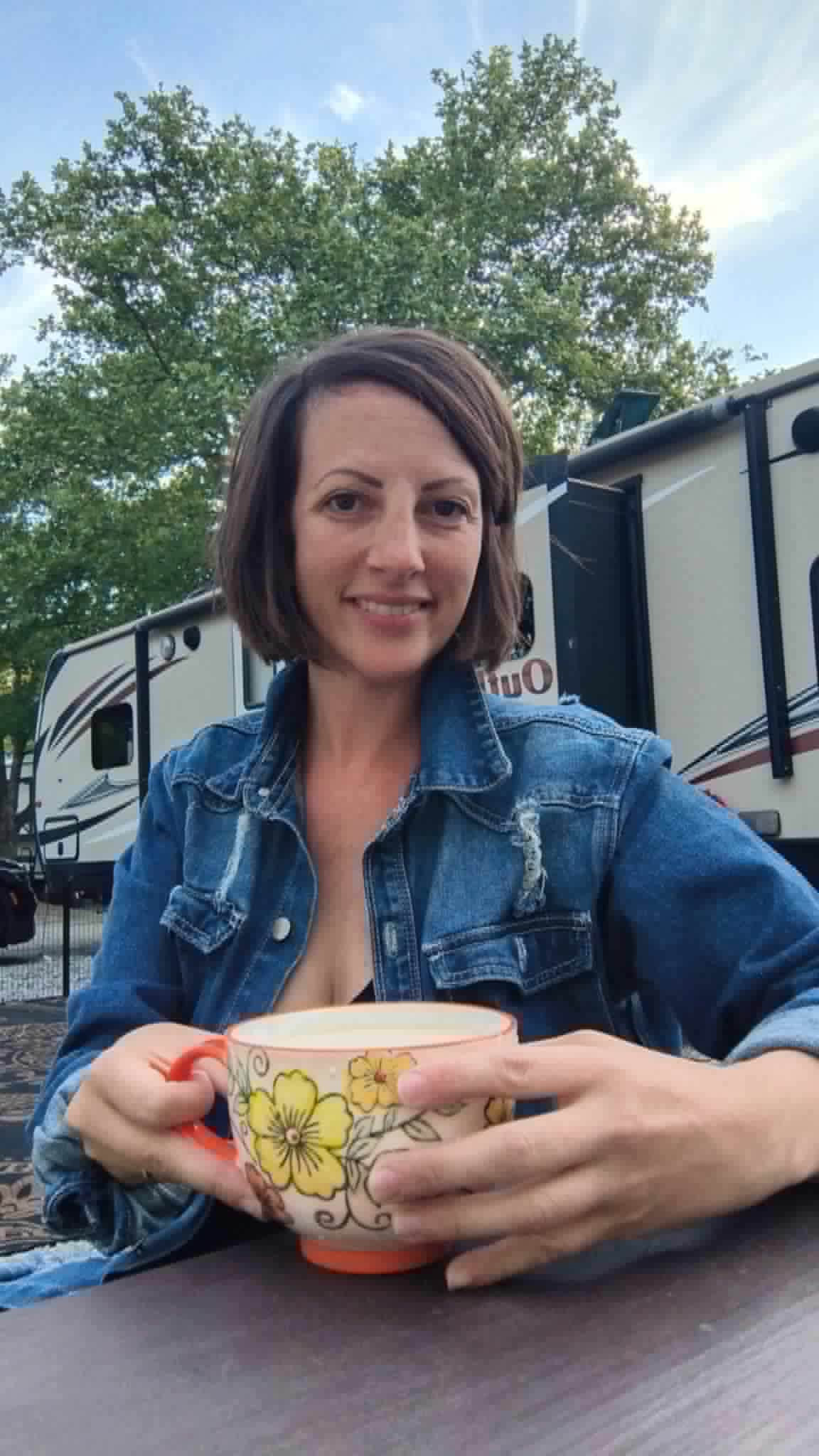 Workamping mom enjoying coffee at RV campsite with travel trailer in background